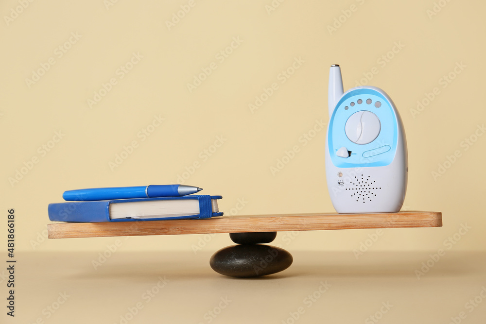 Office supplies with baby monitor on teeterboard against light background. Concept of balance