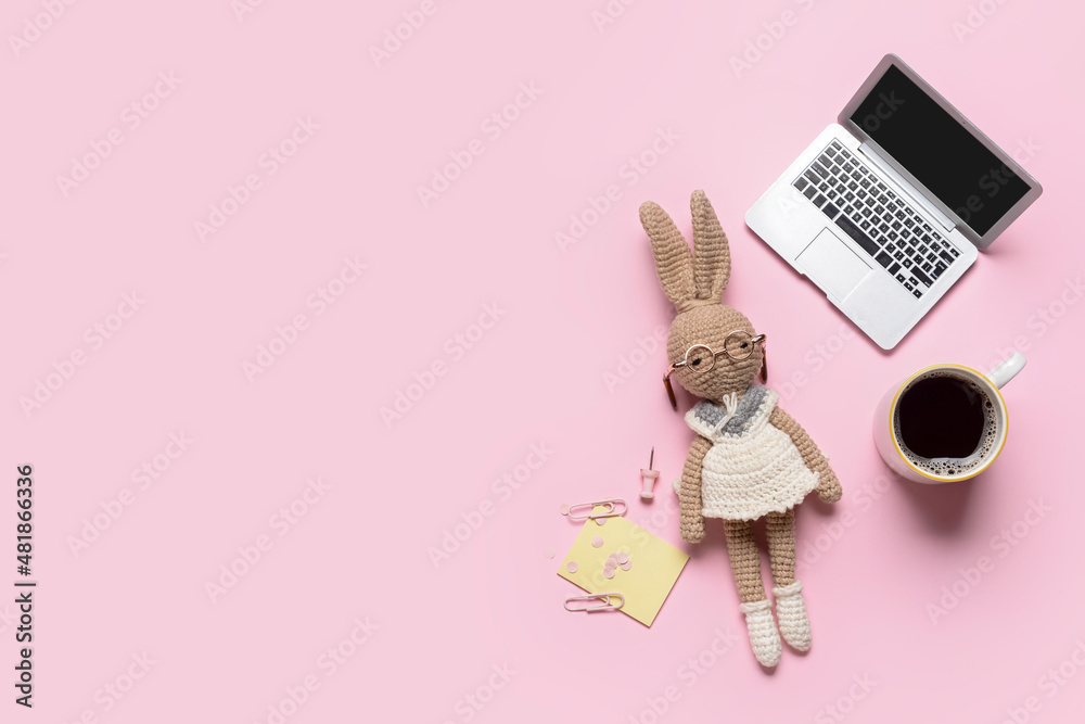 Tiny laptop with bunny toy, cup of coffee and stationery on color background