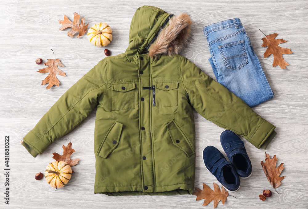 灰色木质背景的保暖儿童夹克、牛仔裤、鞋子和秋季装饰