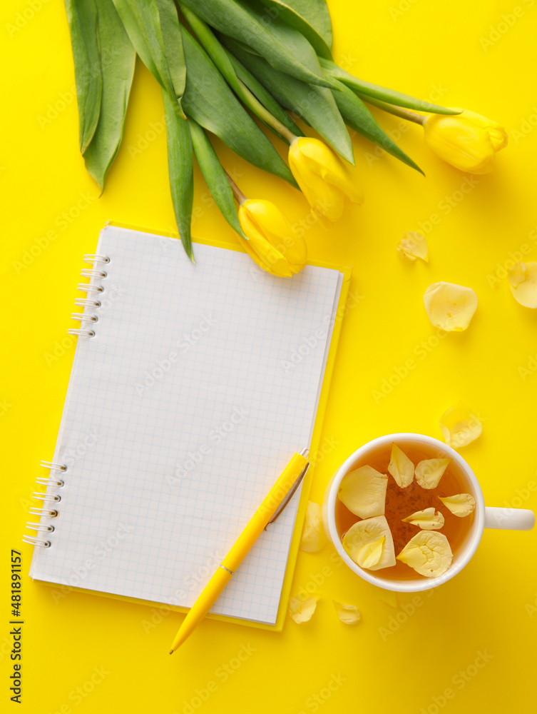 Composition with blank notebook, tulips and cup of tea on yellow background