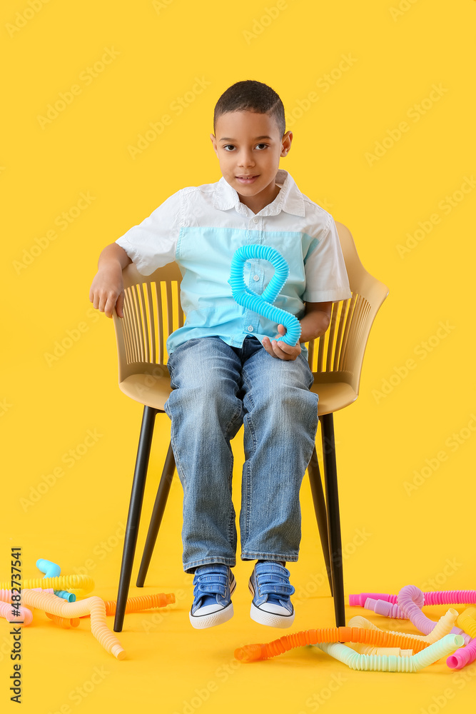 黄色背景下坐在椅子上的戴着Pop Tubes的非裔美国小男孩