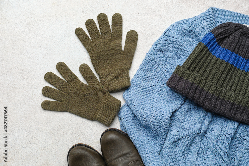 Warm gloves, sweater, hat and shoes on light background, closeup