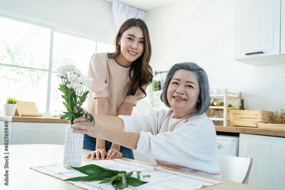 亚洲活跃的老年妇女带着年幼的女儿把花放在花瓶上