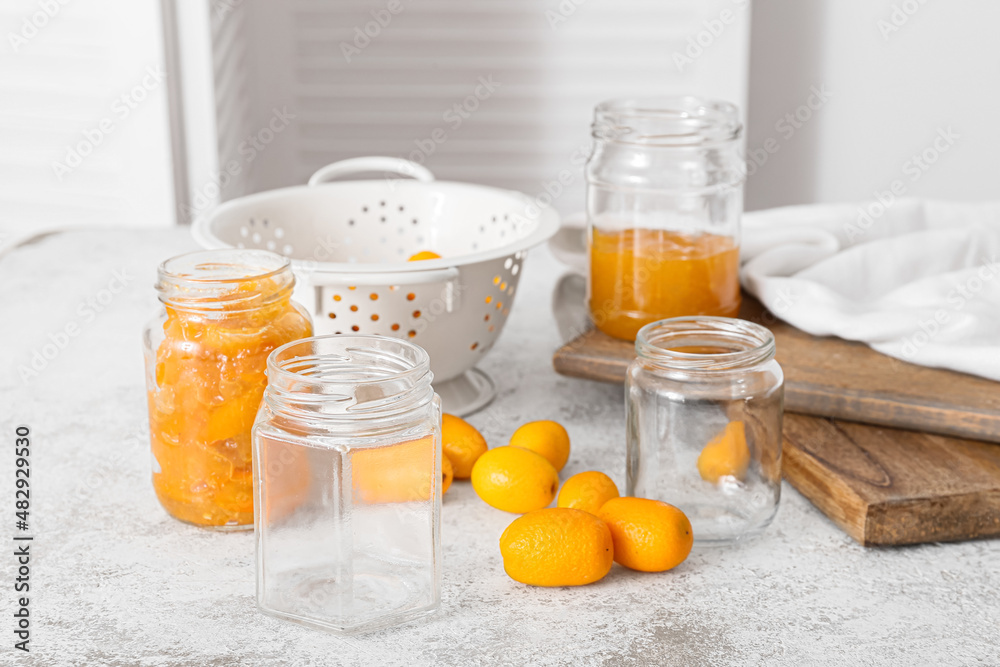 Jars with tasty kumquat jam on kitchen table background
