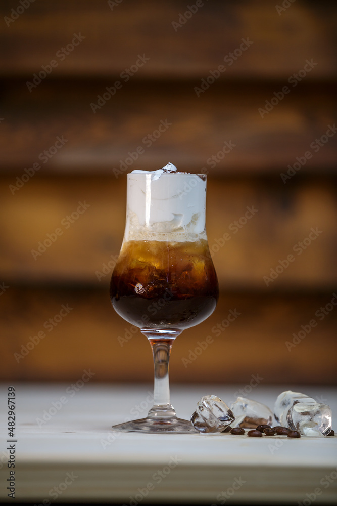Fresh cold coffee and whipped cream in tall glass on table with wood background