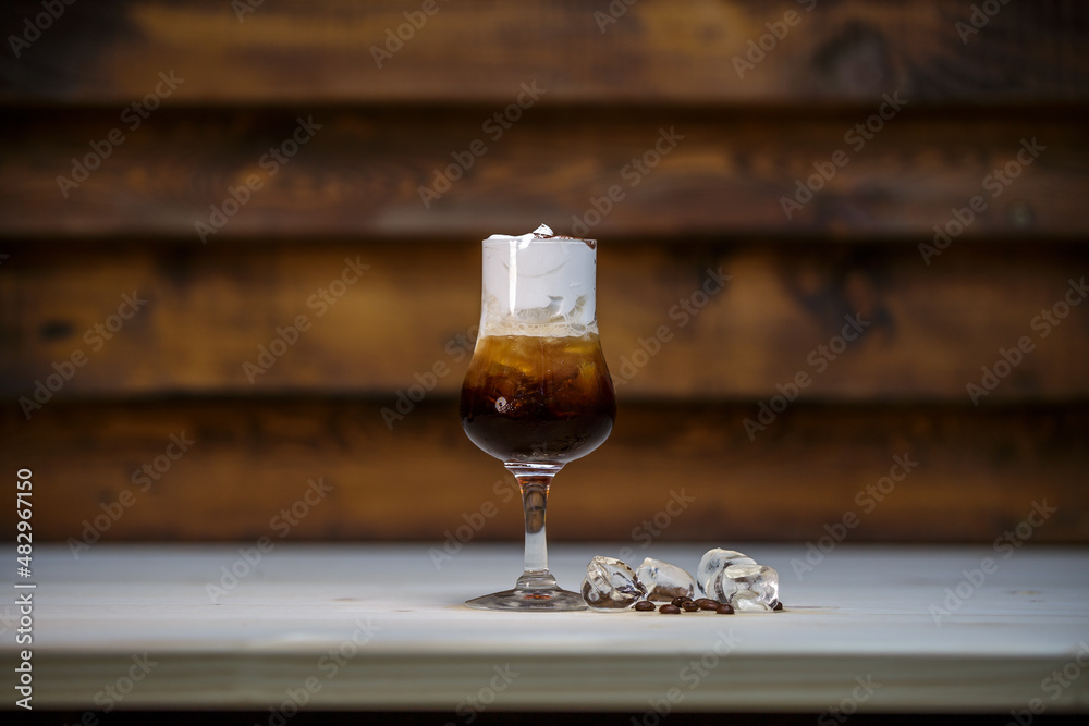Fresh cold coffee and whipped cream in tall glass on table with wood background