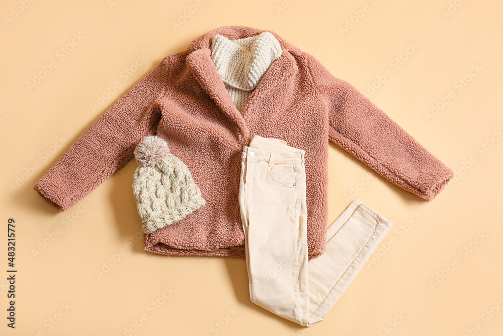 米色背景的冬季外套、毛衣、裤子和针织帽
