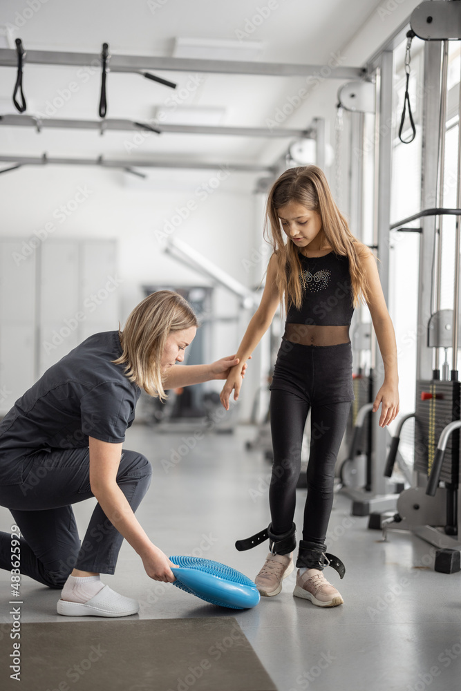Rehabilitation specialist helping little girl to do exercises at gym. Concept of physical therapy fo
