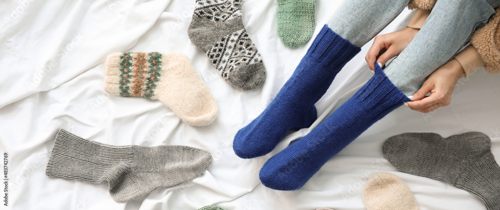 女人在床上穿上保暖的针织袜子。供暖季节的概念