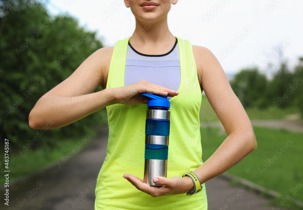 Woman in sportswear holding bottle with protein shake outdoors