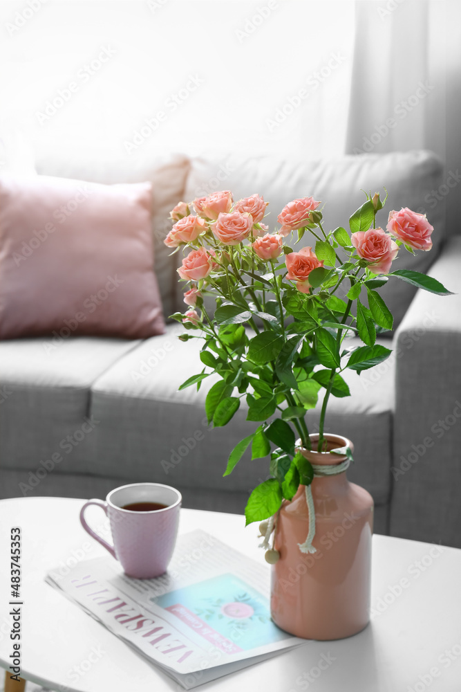 房间桌子上放着漂亮的新鲜玫瑰和一杯咖啡的花瓶