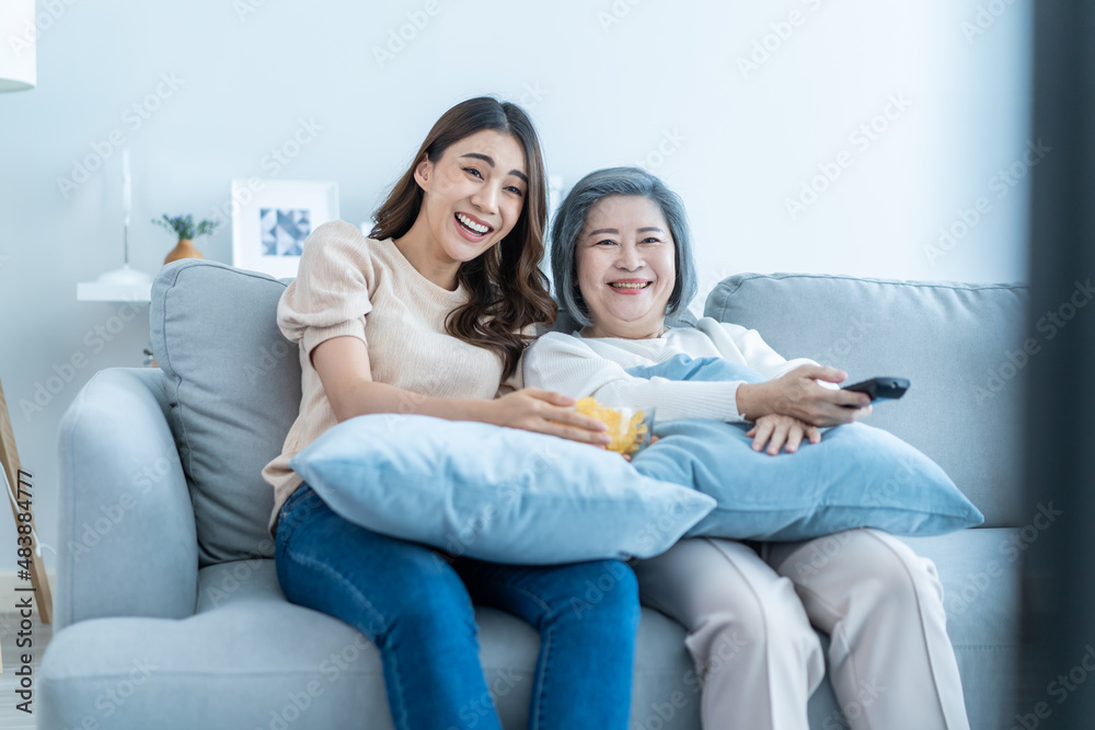 亚洲资深成熟女性和女儿坐在沙发上看搞笑电影。