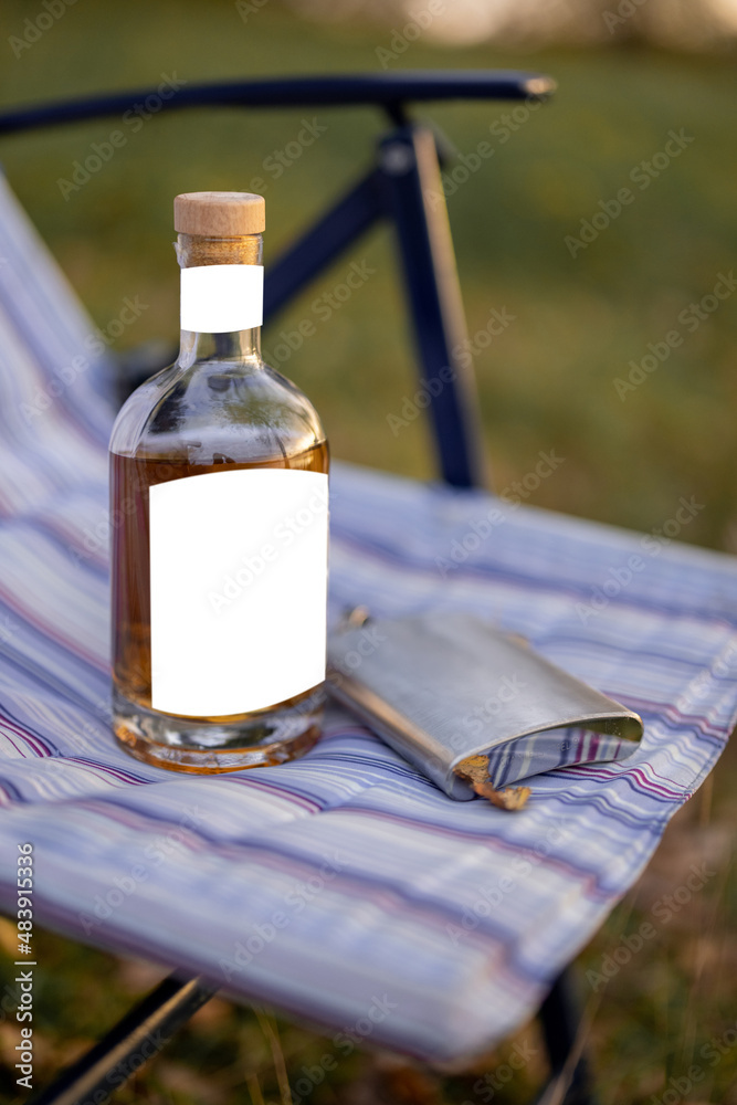 野餐或钓鱼时，装有烈性酒精的瓶子和放在折叠椅上的烧瓶。带有空白标签的瓶子