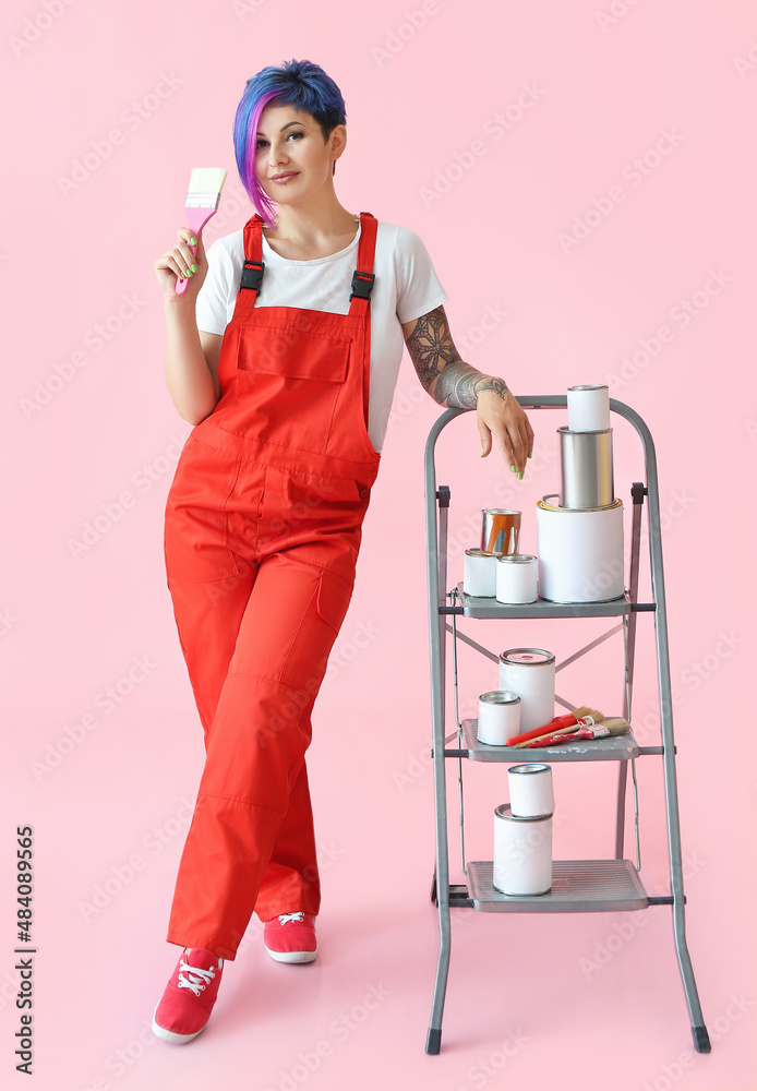 Female painter with brush, ladder and cans on pink background