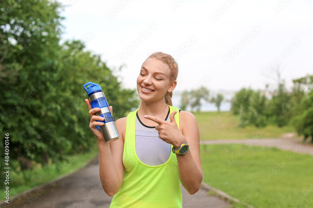 穿着运动服微笑的年轻女子在户外指着一瓶蛋白奶昔