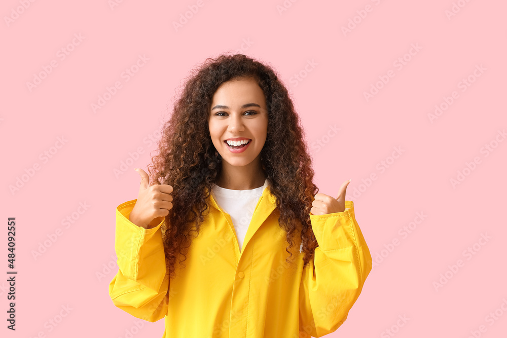 身穿黄色雨衣的年轻非裔美国妇女在粉色背景上竖起大拇指
