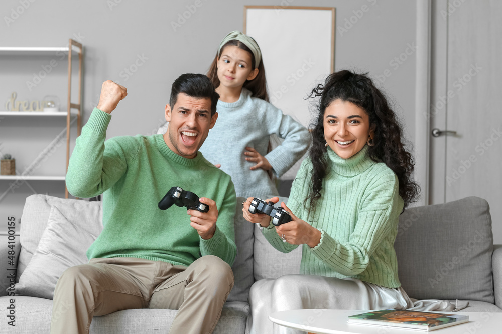 小女儿和穿着保暖毛衣的父母在家玩电子游戏