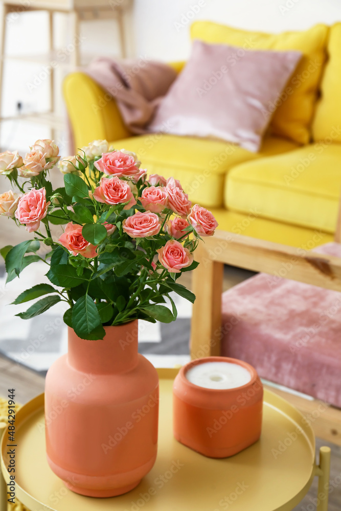 房间桌子上放着一束美丽的新鲜玫瑰和蜡烛的花瓶
