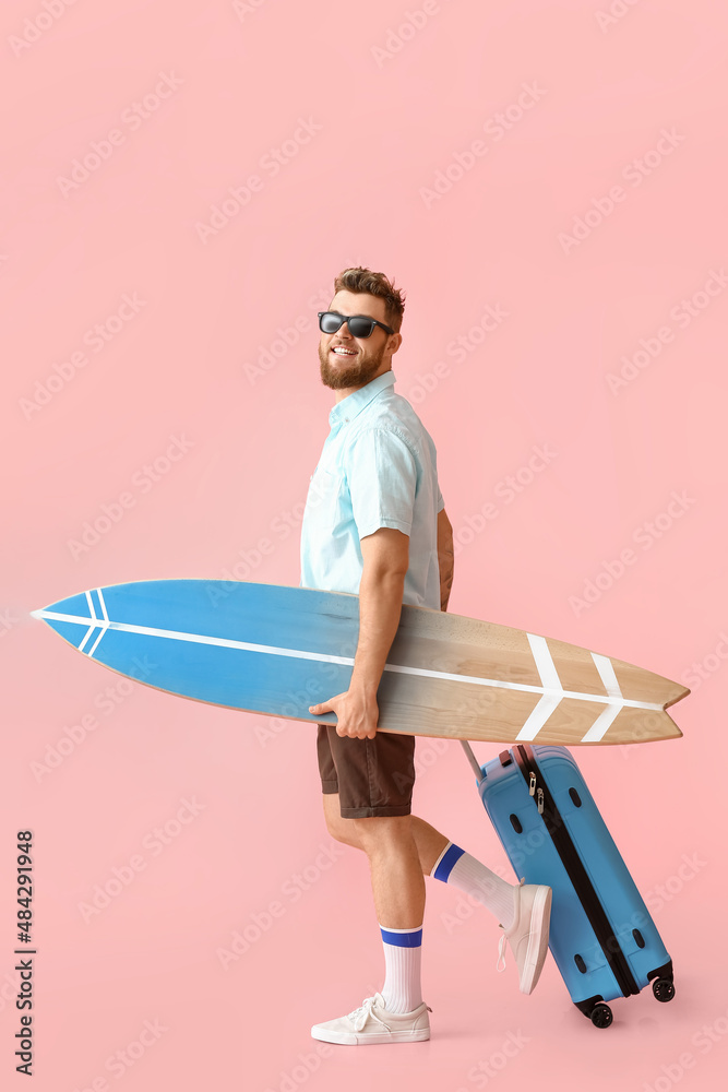 粉色背景带冲浪板和行李箱的英俊男子