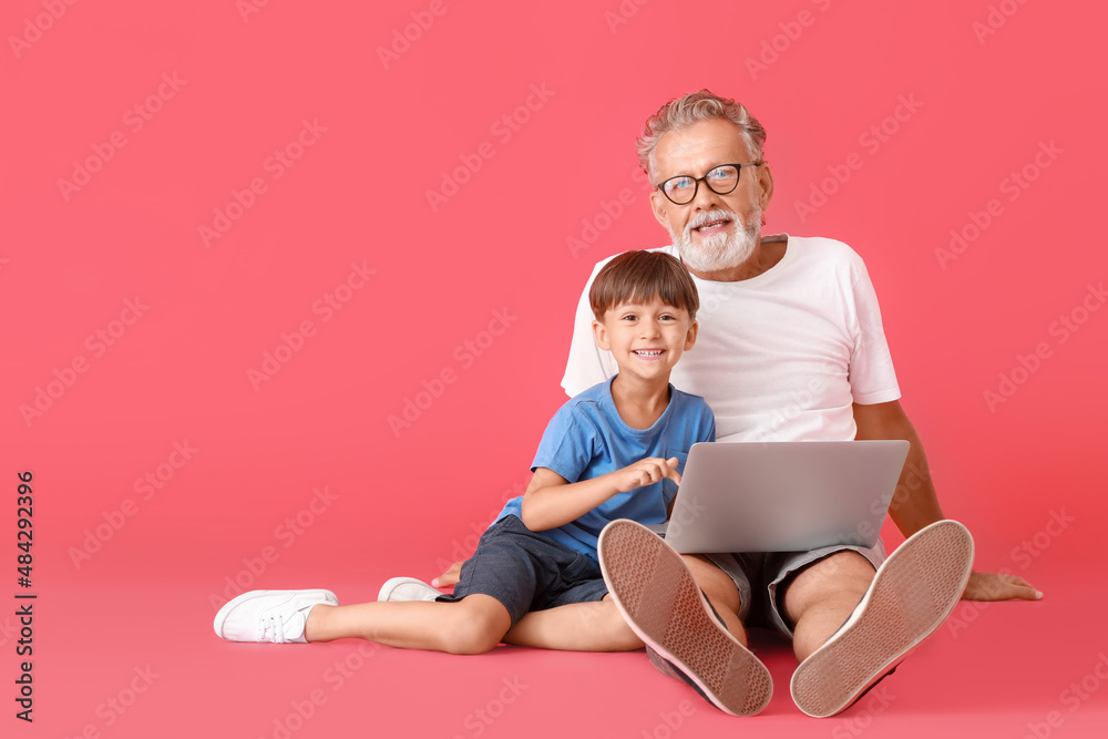 小男孩和他的祖父在红底上使用笔记本电脑