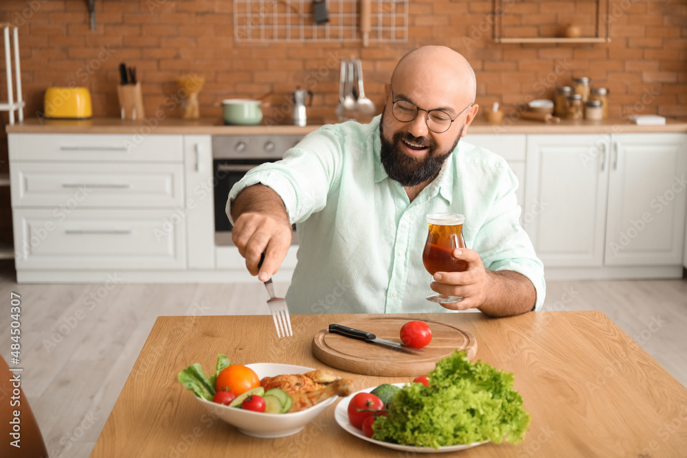Bald man drinking beer and having lunch in kitchen
