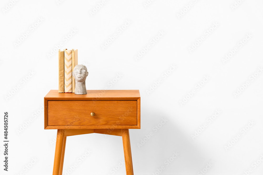 Wooden bedside table with books and decor near light wall