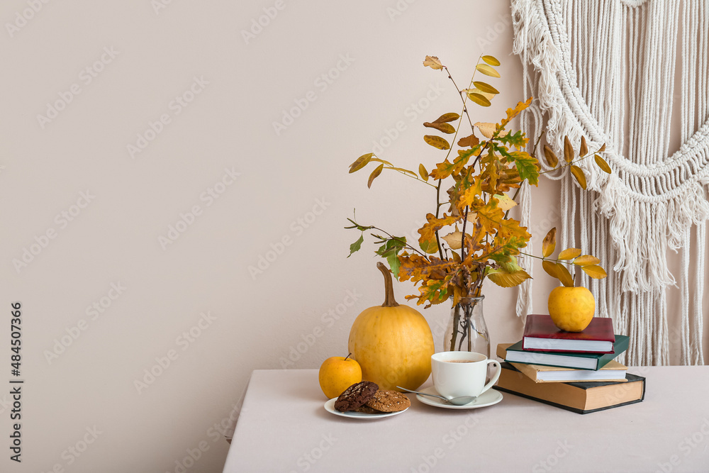 Beautiful composition with autumn branches, pumpkin, books, cup of coffee and plate with cookies on 