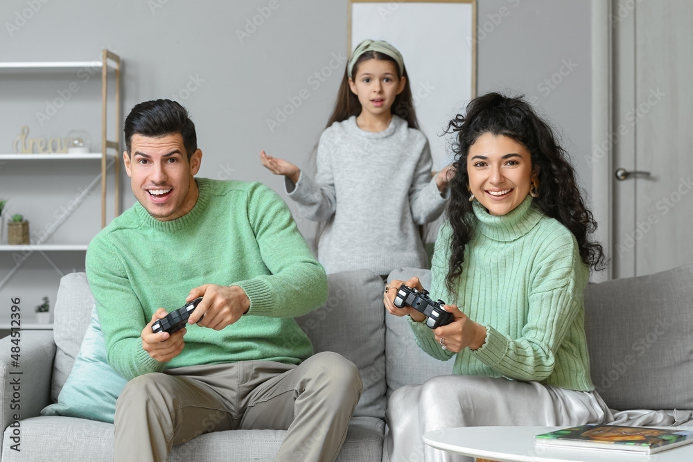 困惑的小女儿和穿着保暖毛衣的父母在家玩电子游戏