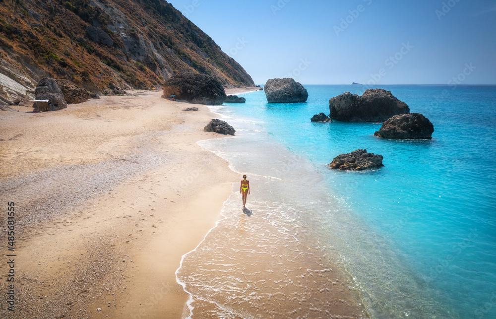 日落时，年轻女子在海边的沙滩上行走，海浪拍打。暑假