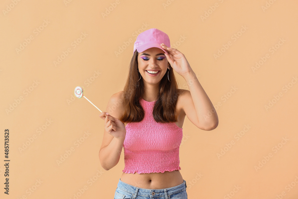 美丽的年轻女子，戴粉色帽子，米色背景上有甜棒棒糖