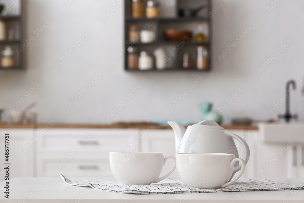 Teapot with cups and napkin on table in light kitchen