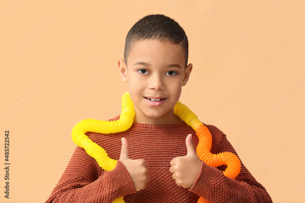 戴着Pop Tubes的非裔美国小男孩在米色背景上竖起大拇指