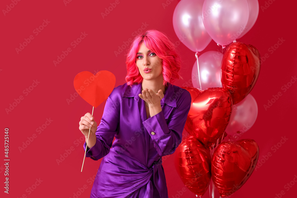 Stylish woman with bright hair, red heart and air balloons sending air kiss on color background. Val