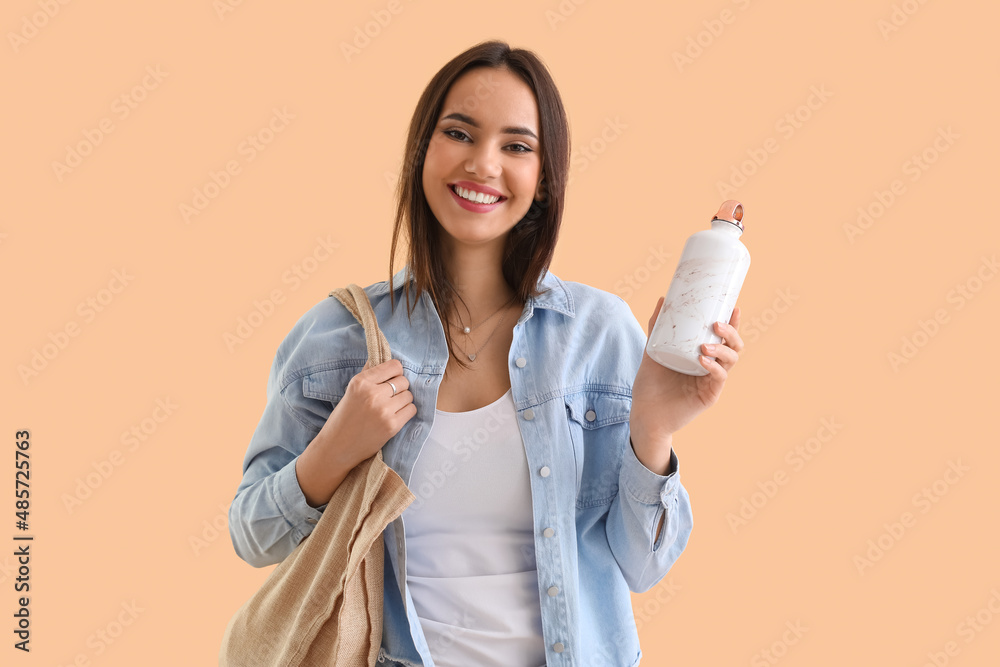 Young woman with eco bag and bottle on beige background
