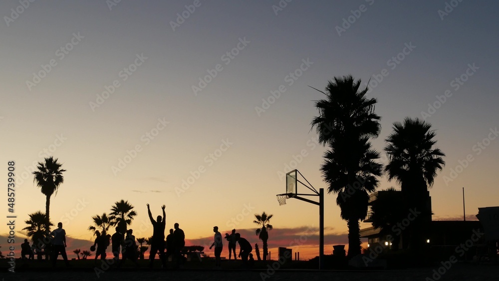 室外篮球场上球员的剪影，人们在打篮球，日落的海洋
