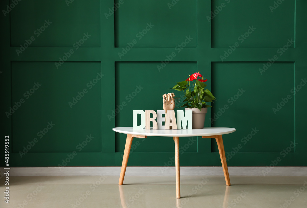 Table with Anthurium flower, wooden hand holding eyeglasses and word DREAM near color wall