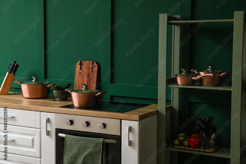 Shelf unit and wooden table with kitchen utensils near color wall