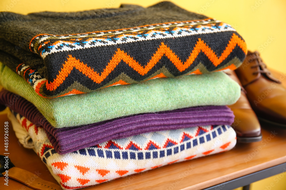 Stack of stylish sweaters on table near color wall, closeup