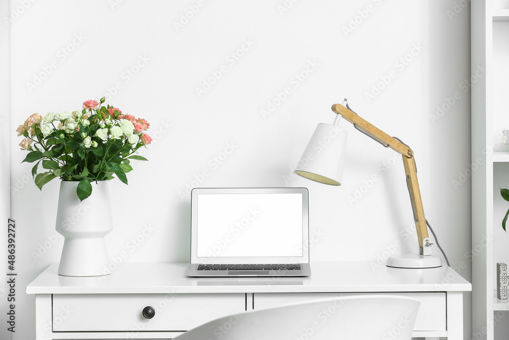 房间桌子上放着一束美丽的新鲜玫瑰和现代笔记本电脑的花瓶