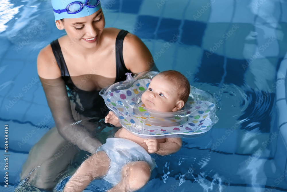年轻女子和她可爱的婴儿在游泳池里带着充气环