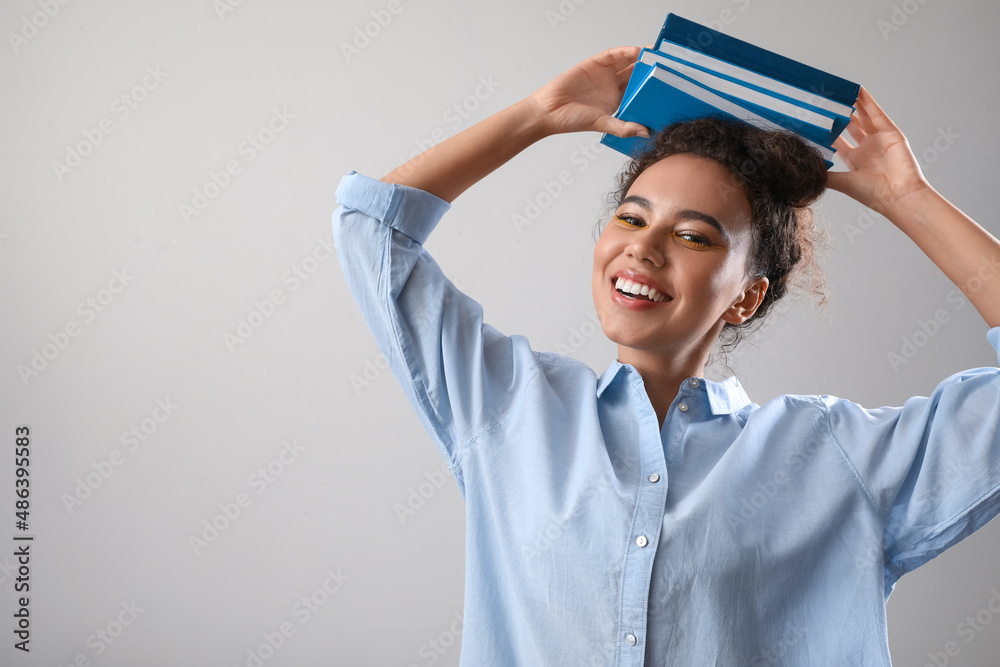 Beautiful young African-American woman with books on grey background