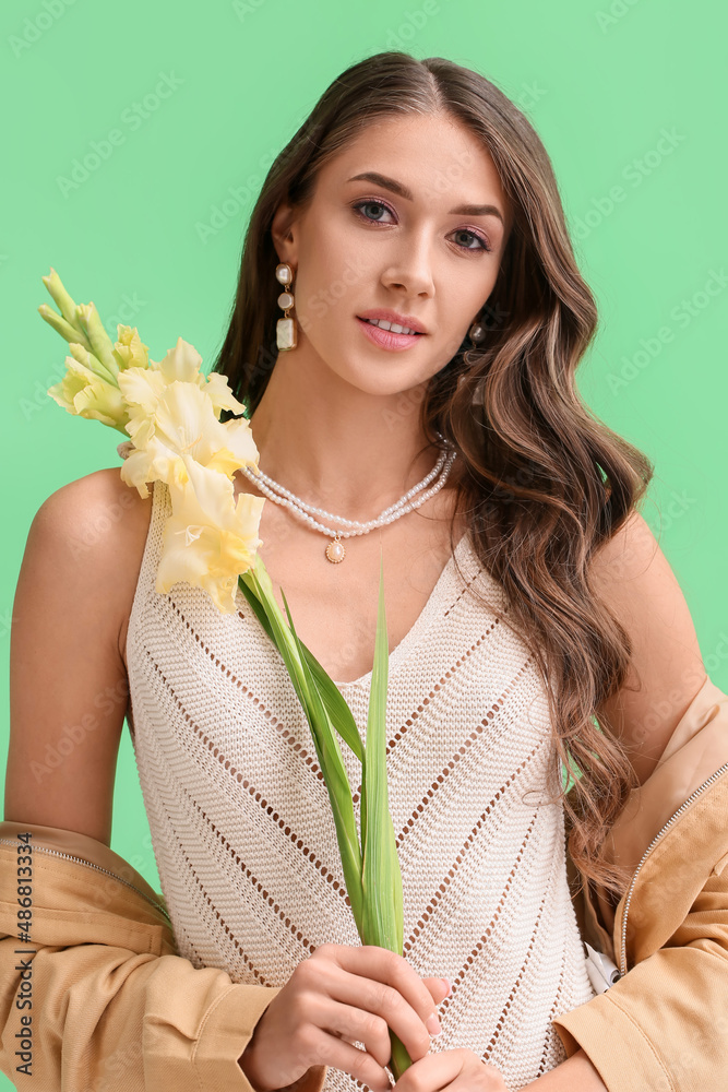 优雅的女人，戴着时尚的珠宝，手里拿着一束绿色背景的唐菖蒲花