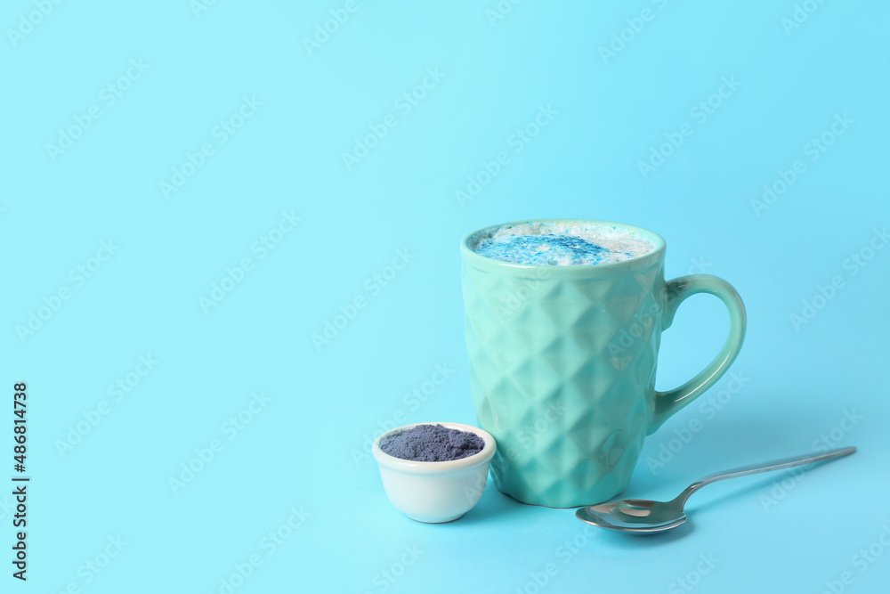 Cup of blue matcha latte and bowl with powder on color background