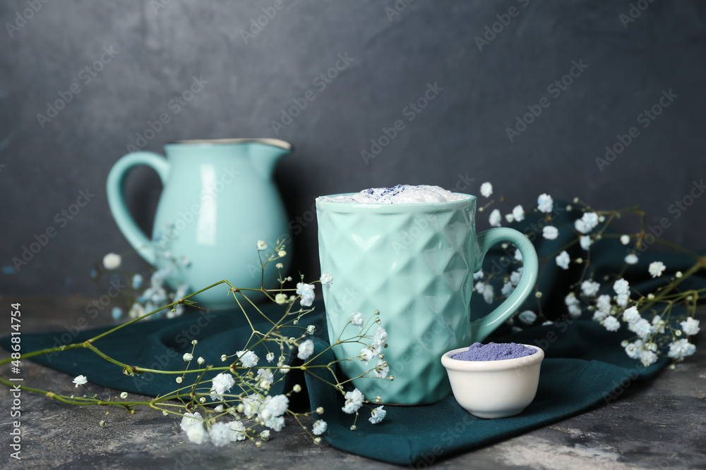 一杯蓝色抹茶拿铁咖啡，黑色背景上的粉末和花朵