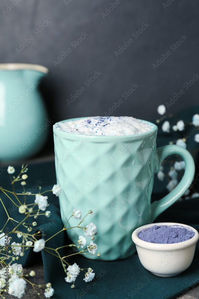 一杯蓝色抹茶拿铁，碗里有粉末和深色背景的花