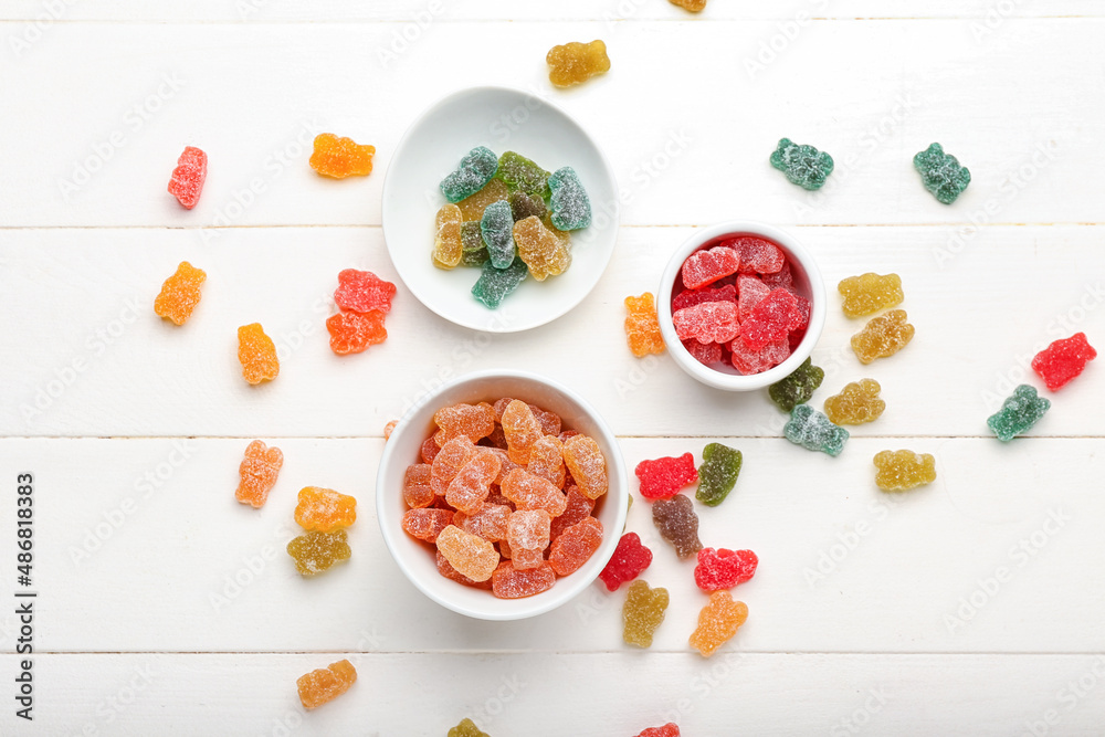 Bowls with different jelly bears on white wooden background