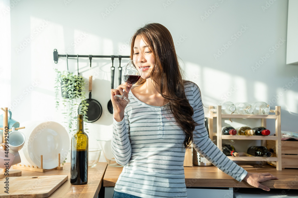 Asian attractive young woman drinking wine in glass in kitchen at home.
