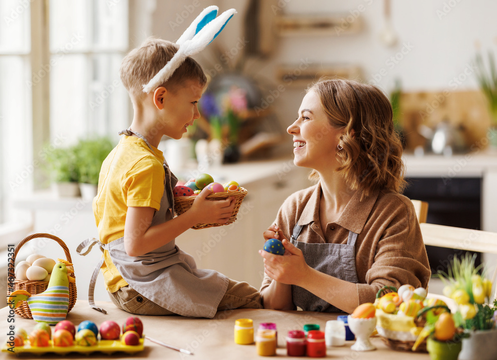 慈爱的年轻母亲坐在厨房里教快乐的小儿子装饰复活节彩蛋