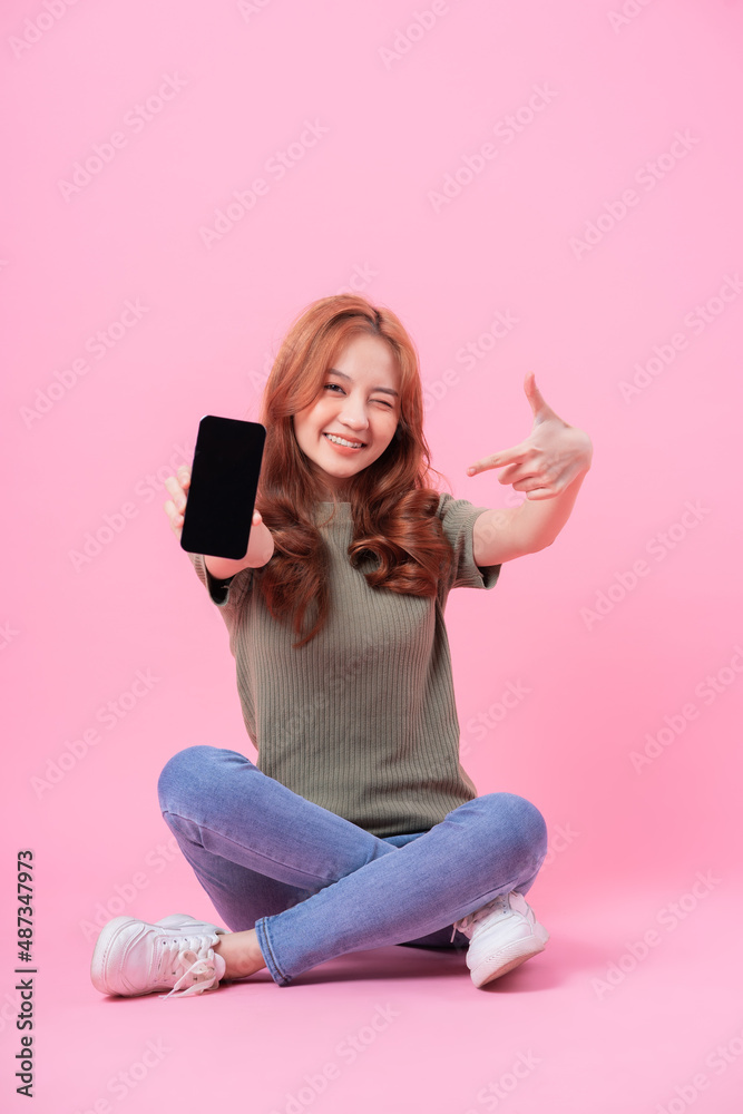 年轻的亚洲女性坐在粉色背景下使用智能手机