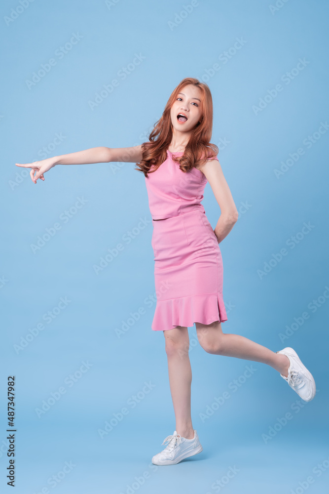 身穿粉色连衣裙，在蓝色背景下摆姿势的年轻亚洲女性